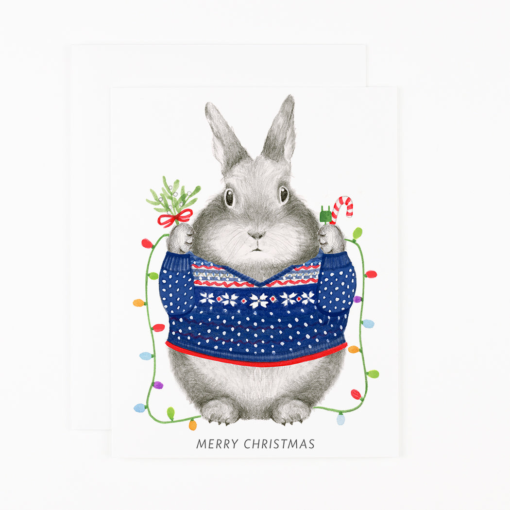 An illustration of a Christmas Bunny wearing a Christmas sweater and holding a branch and candy cane, surrounded by mistletoe lights by Dear Hancock.