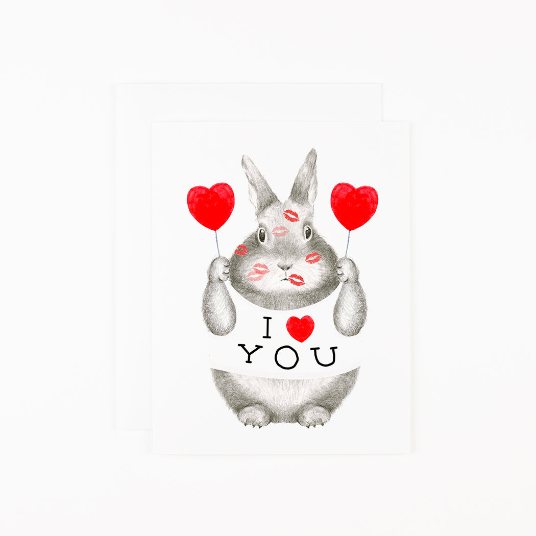 Hand-drawn graphite bunny with kisses on his face, holding two heart-shaped balloons wearing a t-shirt that reads, &quot;I heart you&quot; 