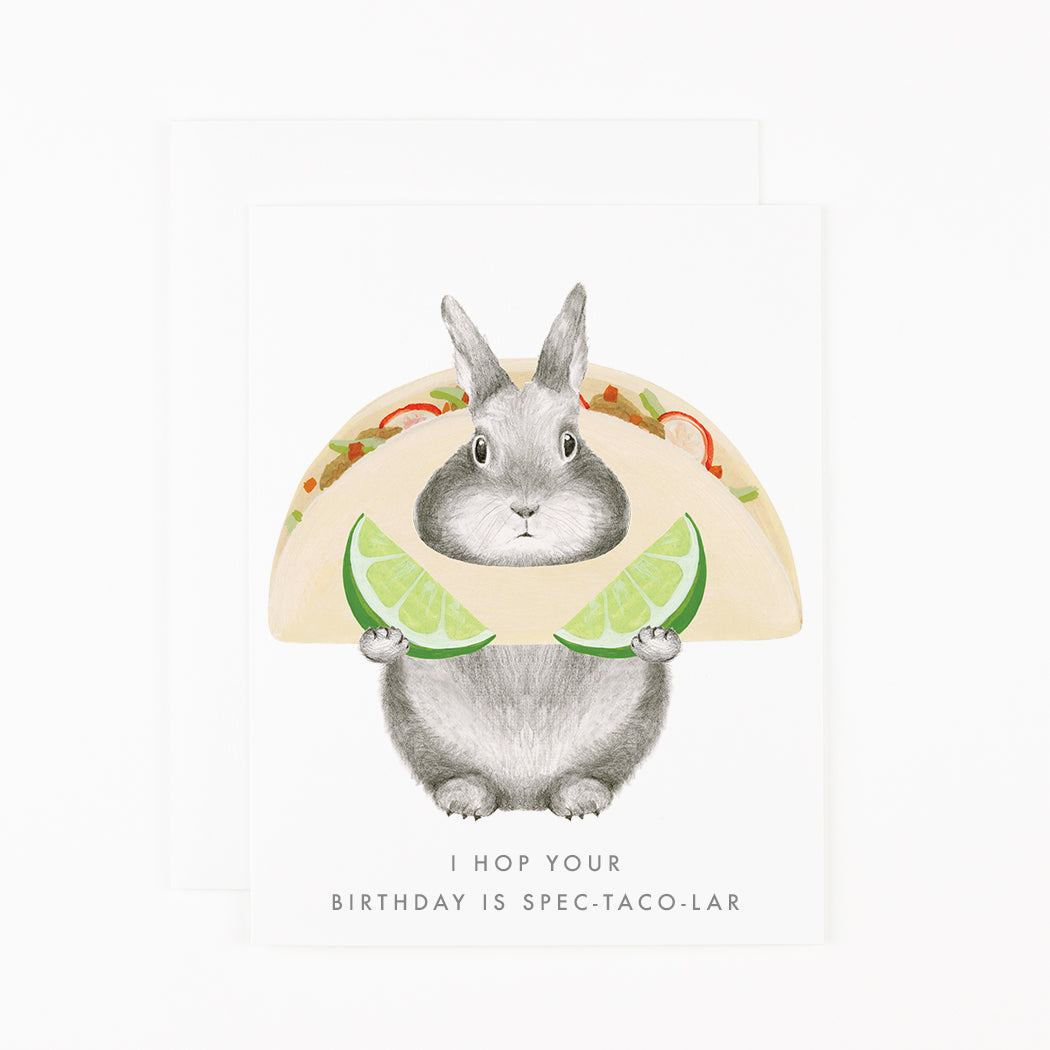 A Spec-Taco-Lar card by Dear Hancock, featuring a cute bunny holding a taco, made in the United States of America. This card is printed on soft white paper, creating a high-quality and visually pleasing design. Perfect.