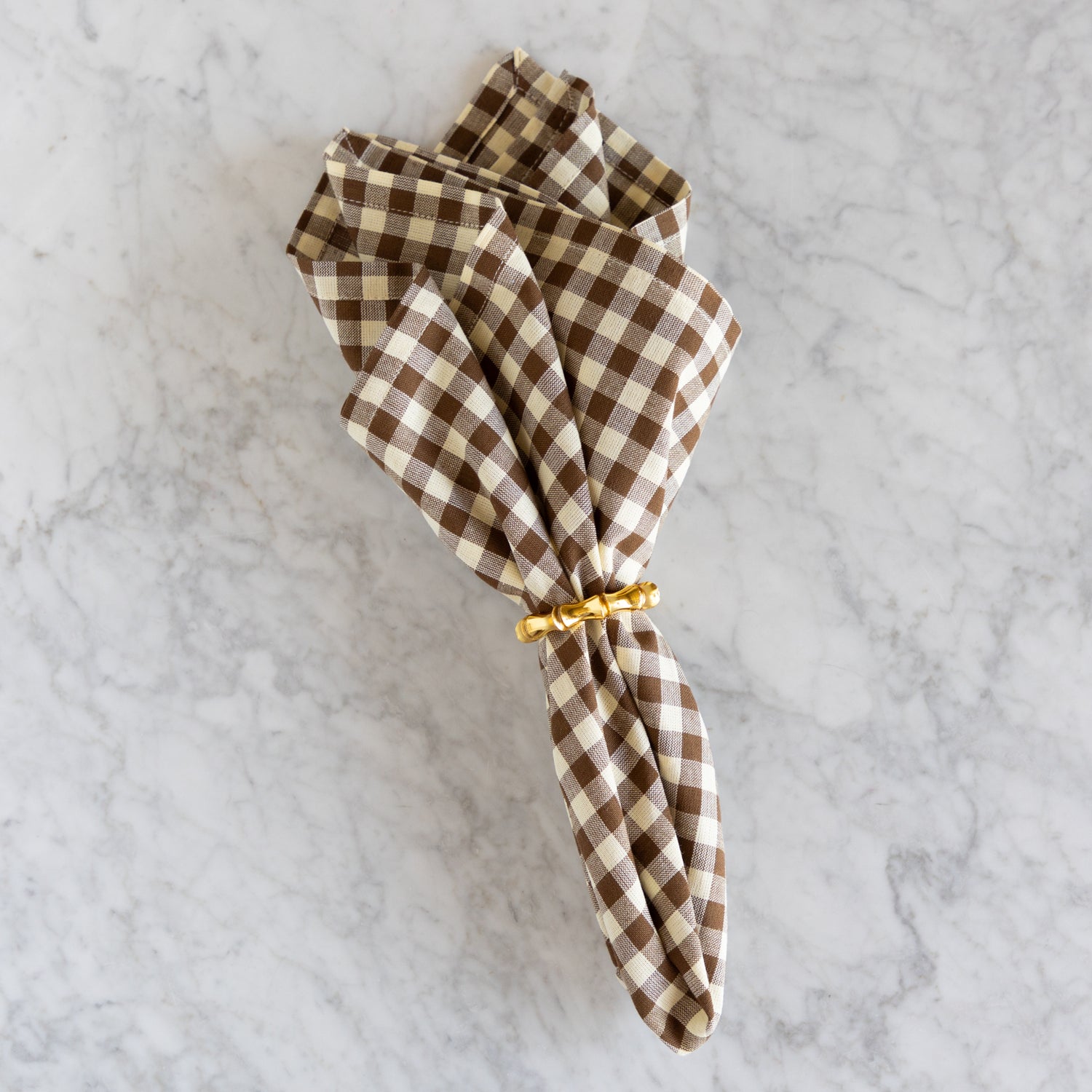 Folded brown and white checkered napkin with a gold napkin ring on a marble surface.