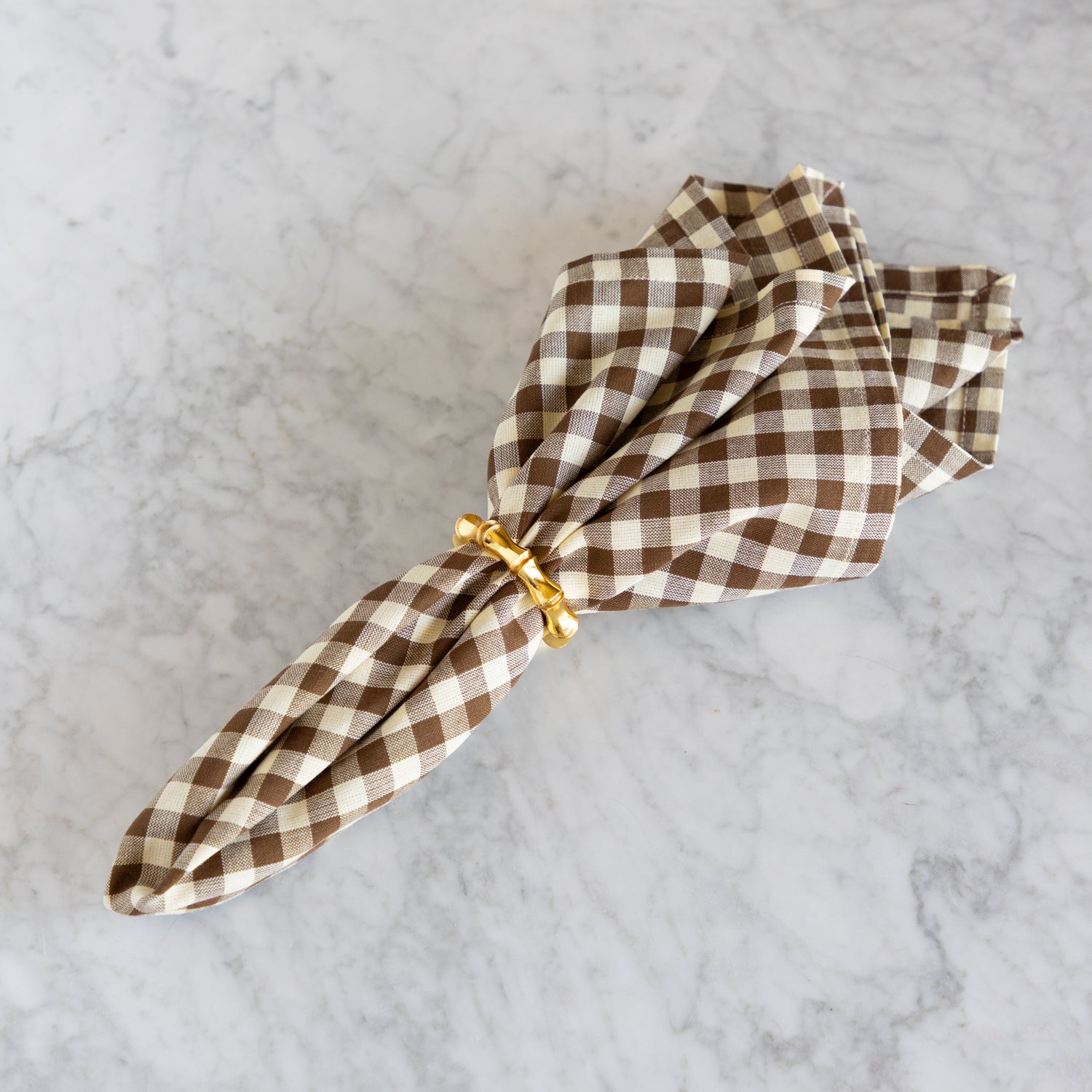 Folded brown and white checkered napkin with a gold ring on a marble surface.