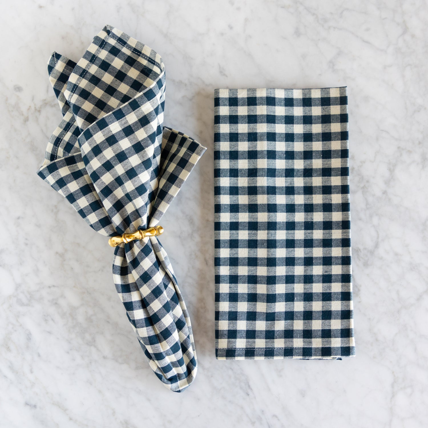 Blue and white checkered napkin with a gold napkin ring on a marble surface.
