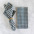 Blue and white checkered napkin with a gold napkin ring on a marble surface.