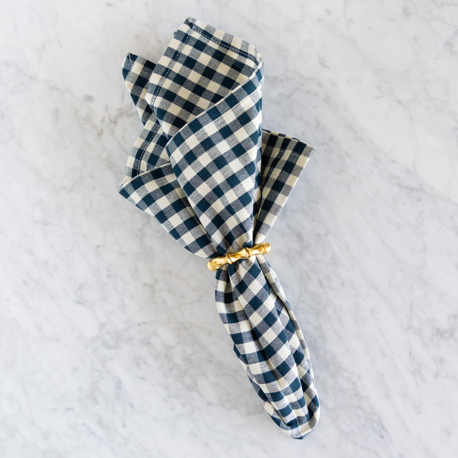 Blue and white checkered napkin with a gold tie on a light gray background.