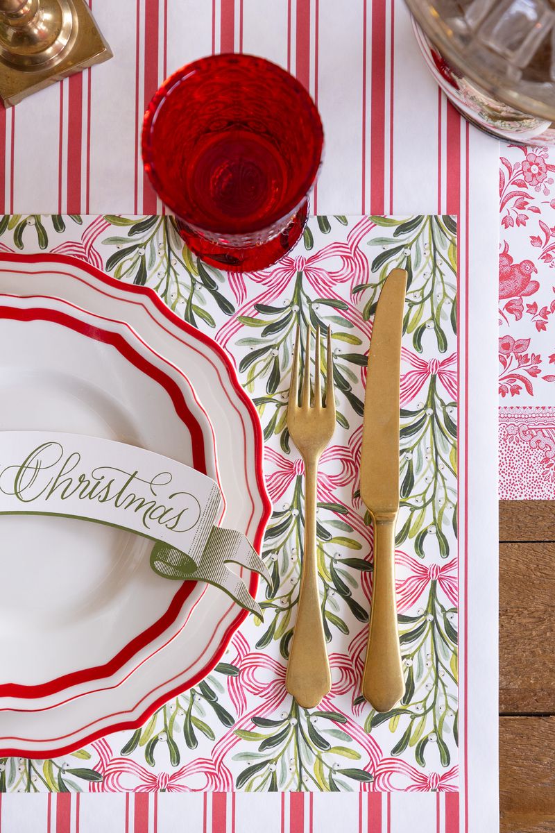 A holiday tablescape featuring the mistletoe placemat on a red and white striped runner.
