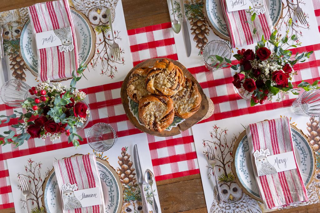 Decorative table setting with red and white checkered tablecloth, owl-themed placemats, and floral arrangements.