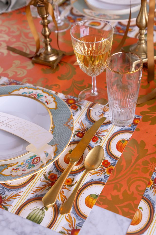 Dining table setting with decorative plates, glasses, and cutlery on a patterned tablecloth.