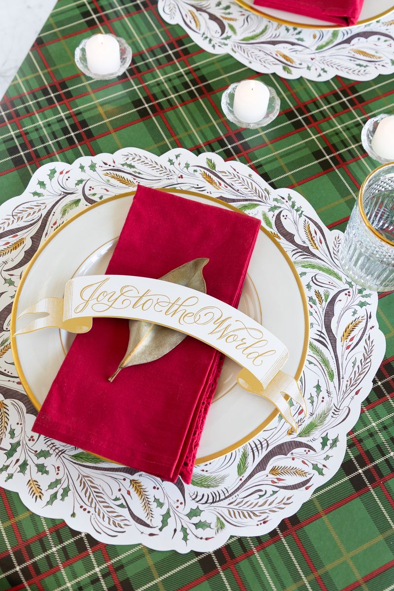 A paper Joy To The World Table Accent laid across the red napkin of a holiday place setting.