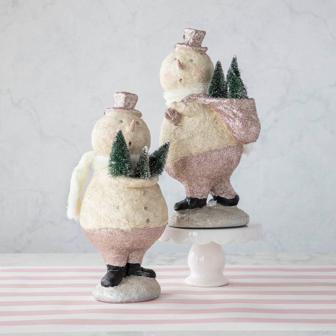 Two Sparkle Snowman figurines, one carrying trees on its back and one holding trees in its arms.