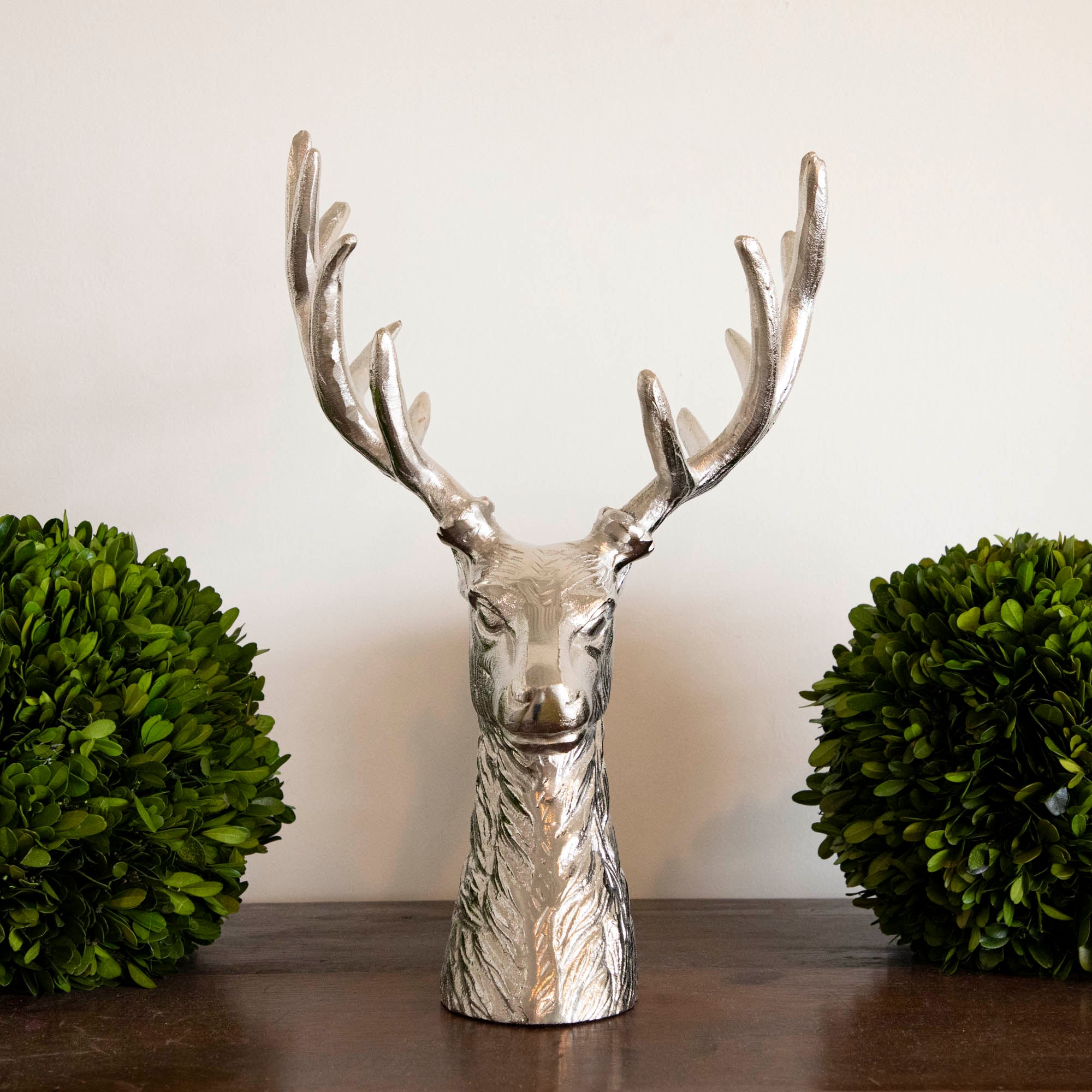 An aluminum Reindeer Bust between two boxwood balls, on mantle.