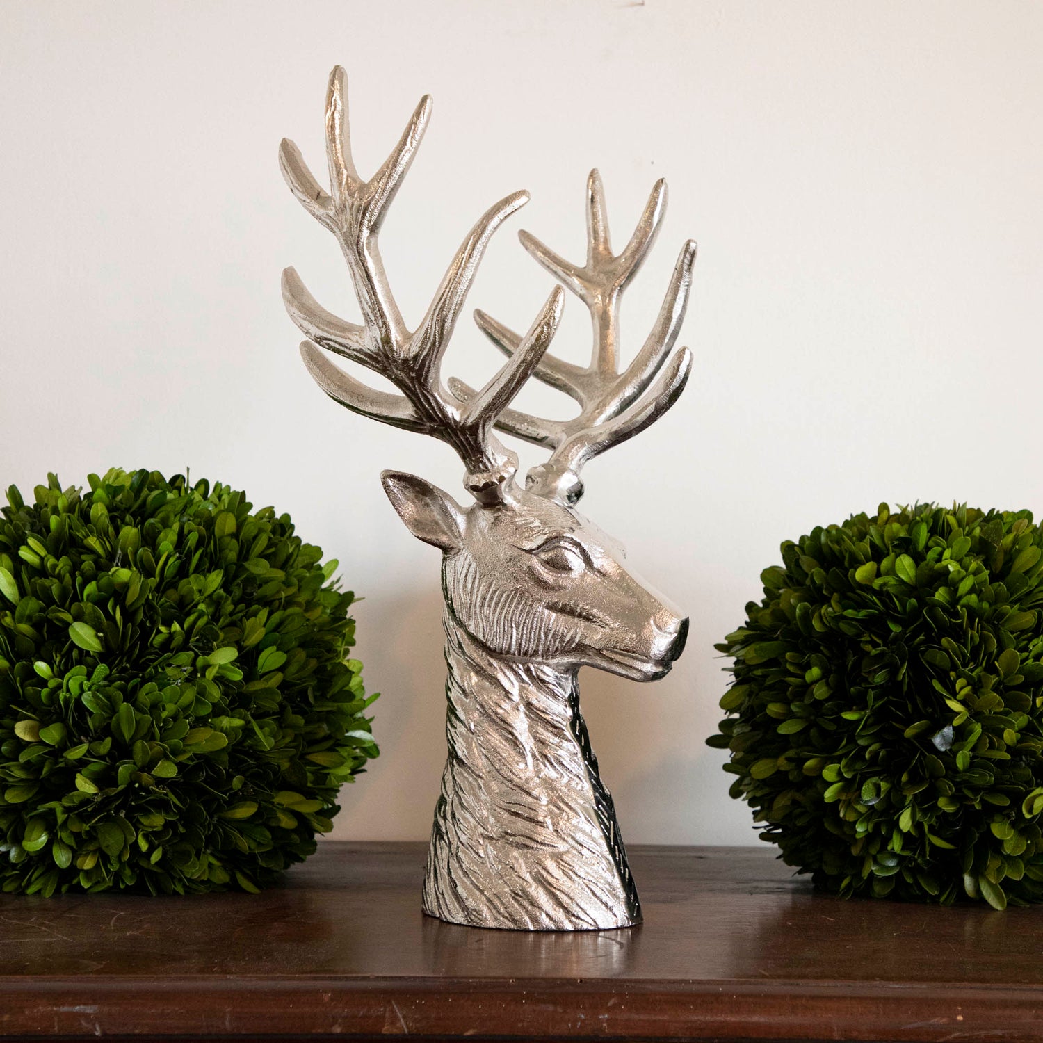 An aluminum Reindeer Bust between two boxwood balls, on mantle.