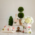 Decorative indoor setting with Laura Stoddart drawstring bags in floral patterns, topiary plants, and a vase of white hydrangeas on a table from Hester & Cook.