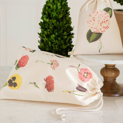 Two of the Laura Stoddart Drawstring Bags resting on a white table with potted plants.