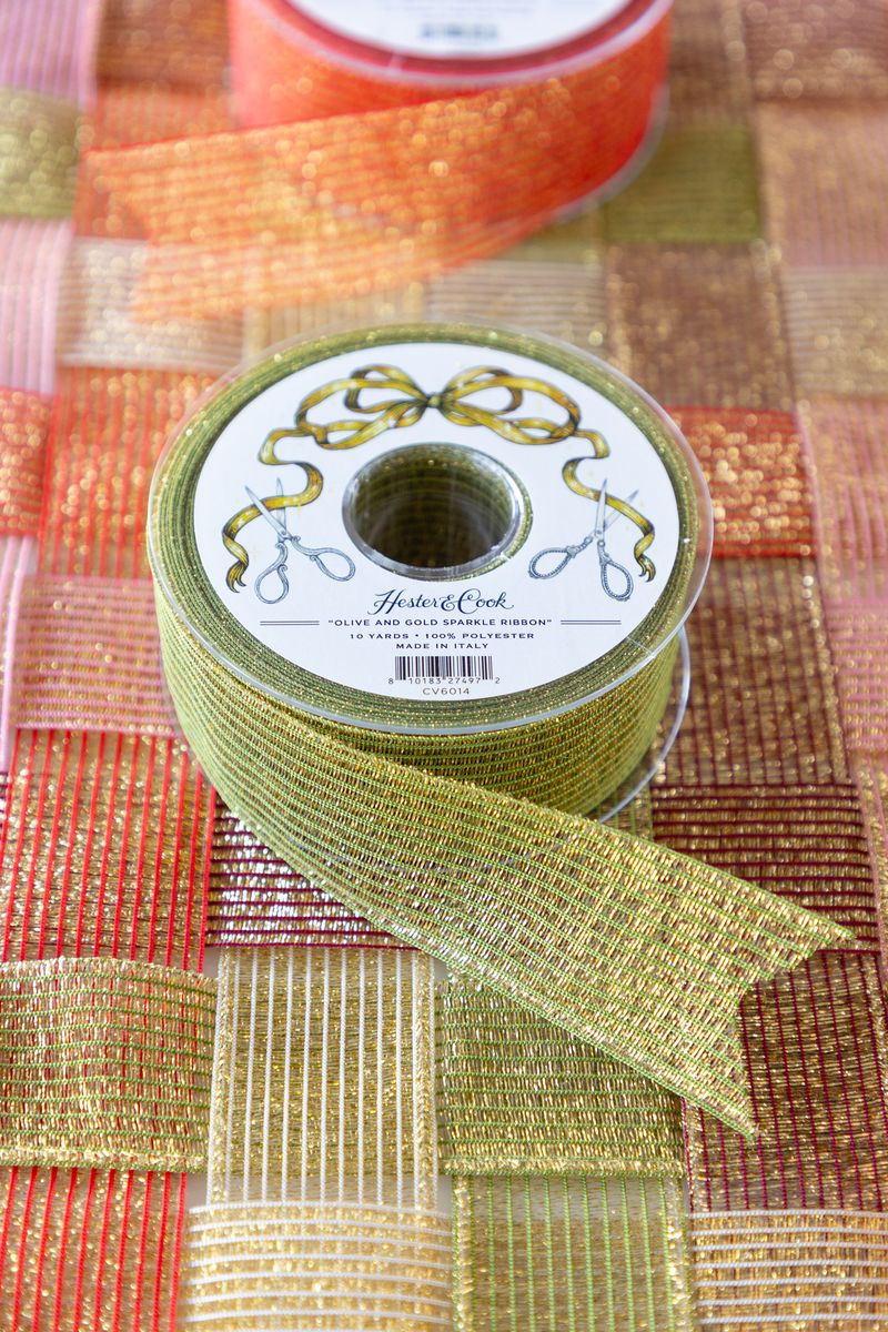 A spool of sparkly green and gold ribbon on a surface of woven sparkle ribbon in five different colors. 
