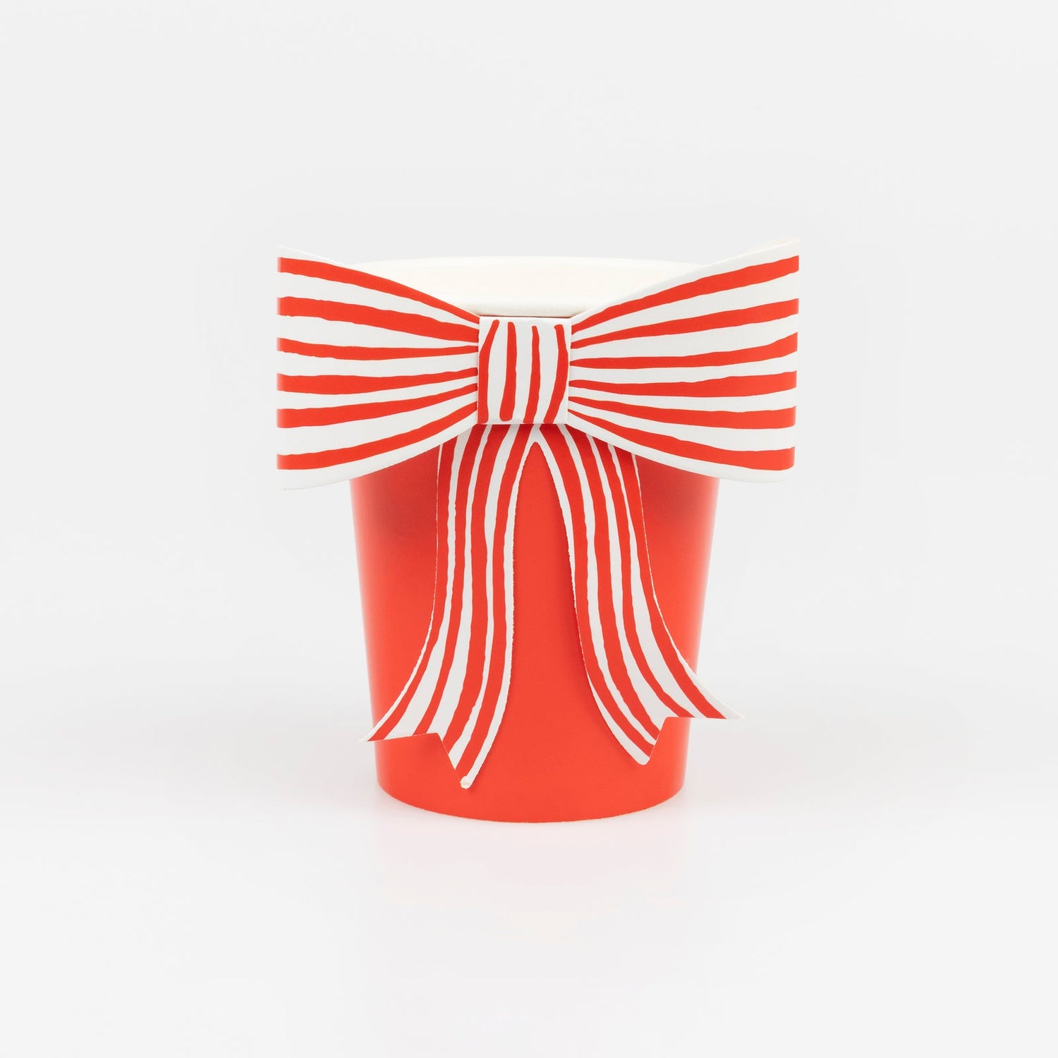 A red paper cup by Meri Meri with a white and red striped paper bow on it.