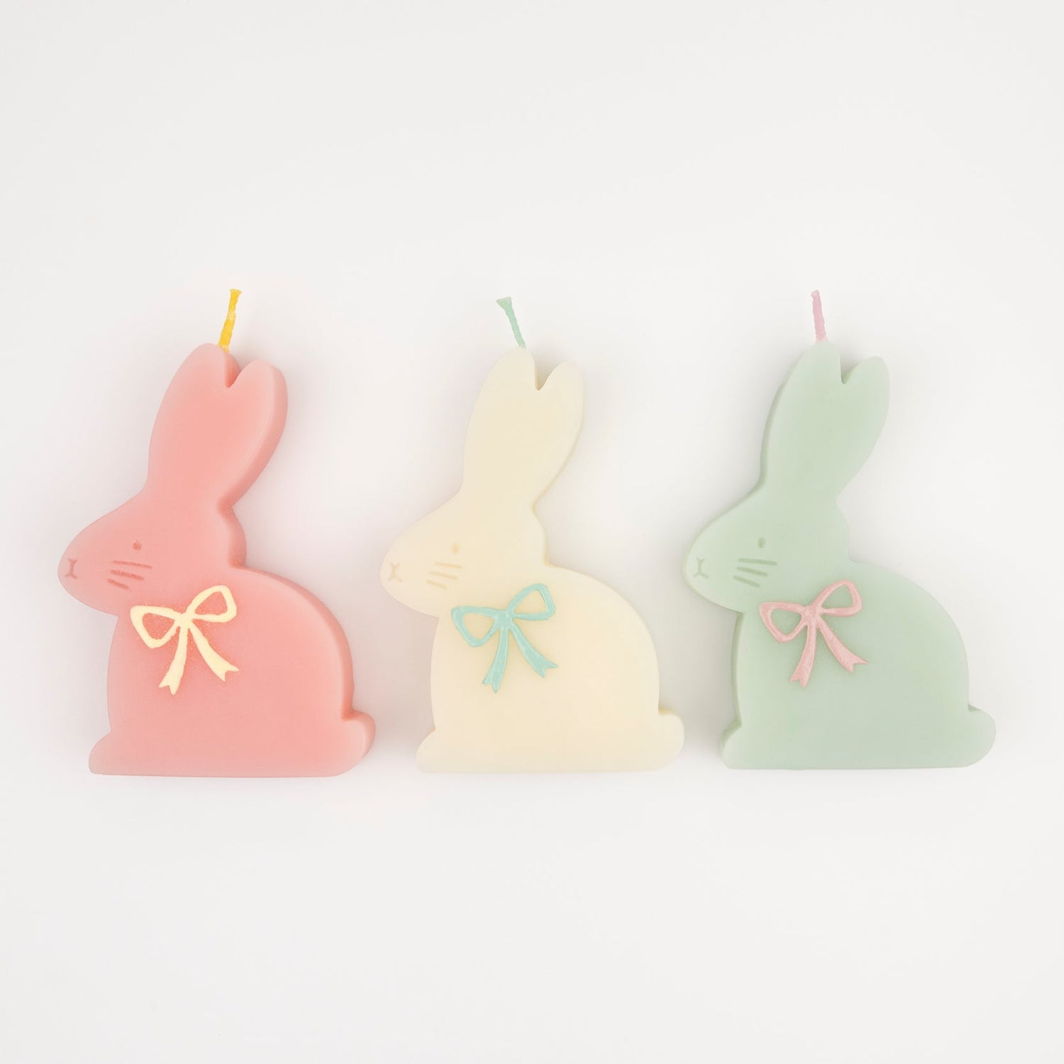 Three bunny-shaped candles in pastel colors with embossed faces and hand-painted bows.