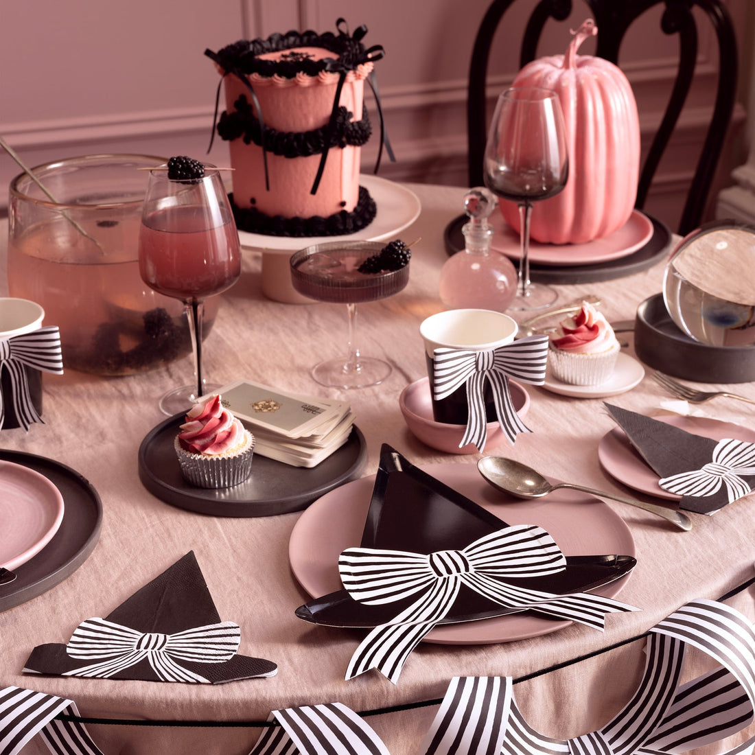 Decorative table setting with black and white bow accents, pink cake, and wine glasses.