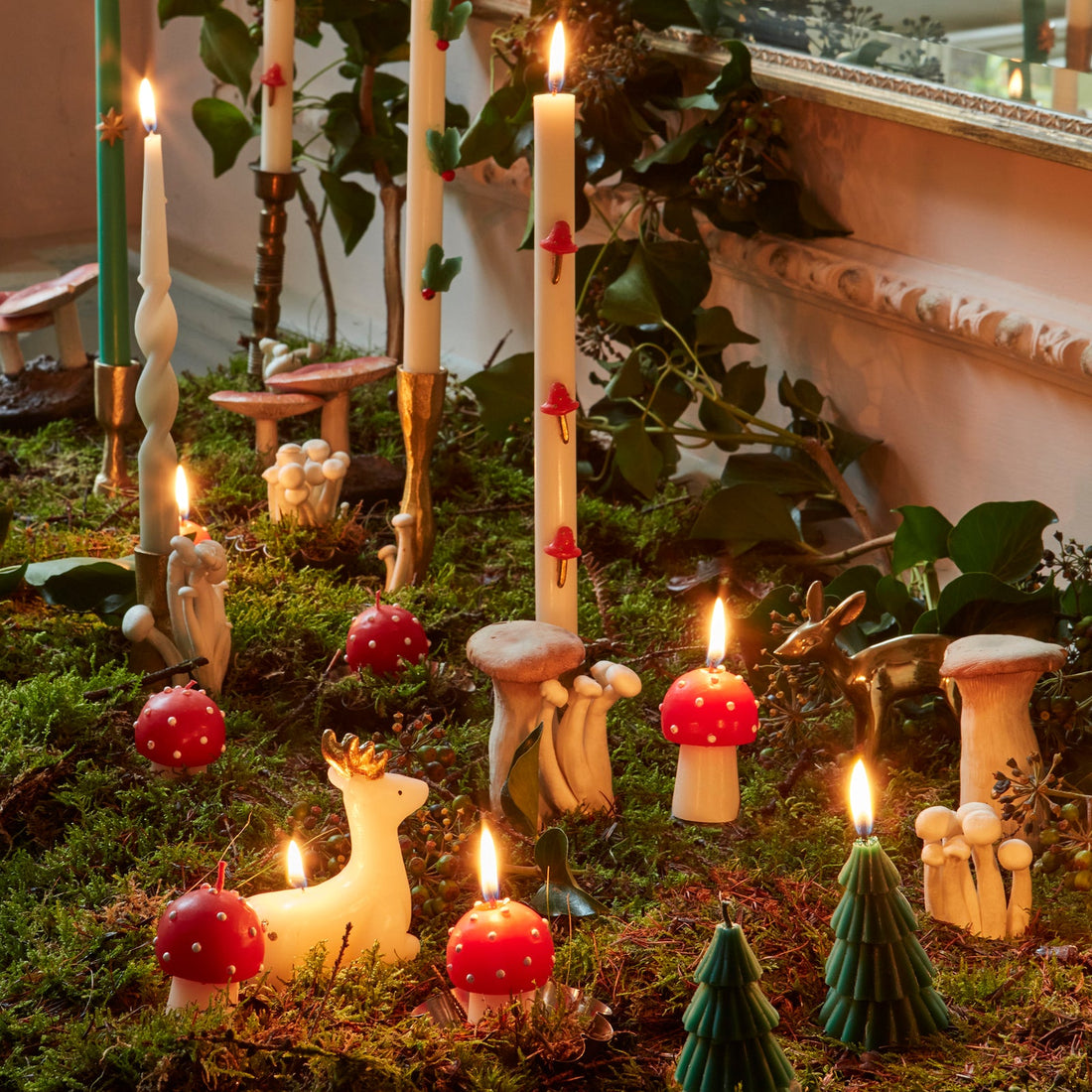 Fairy garden with candles, mushrooms, and small figurines on a grassy surface.