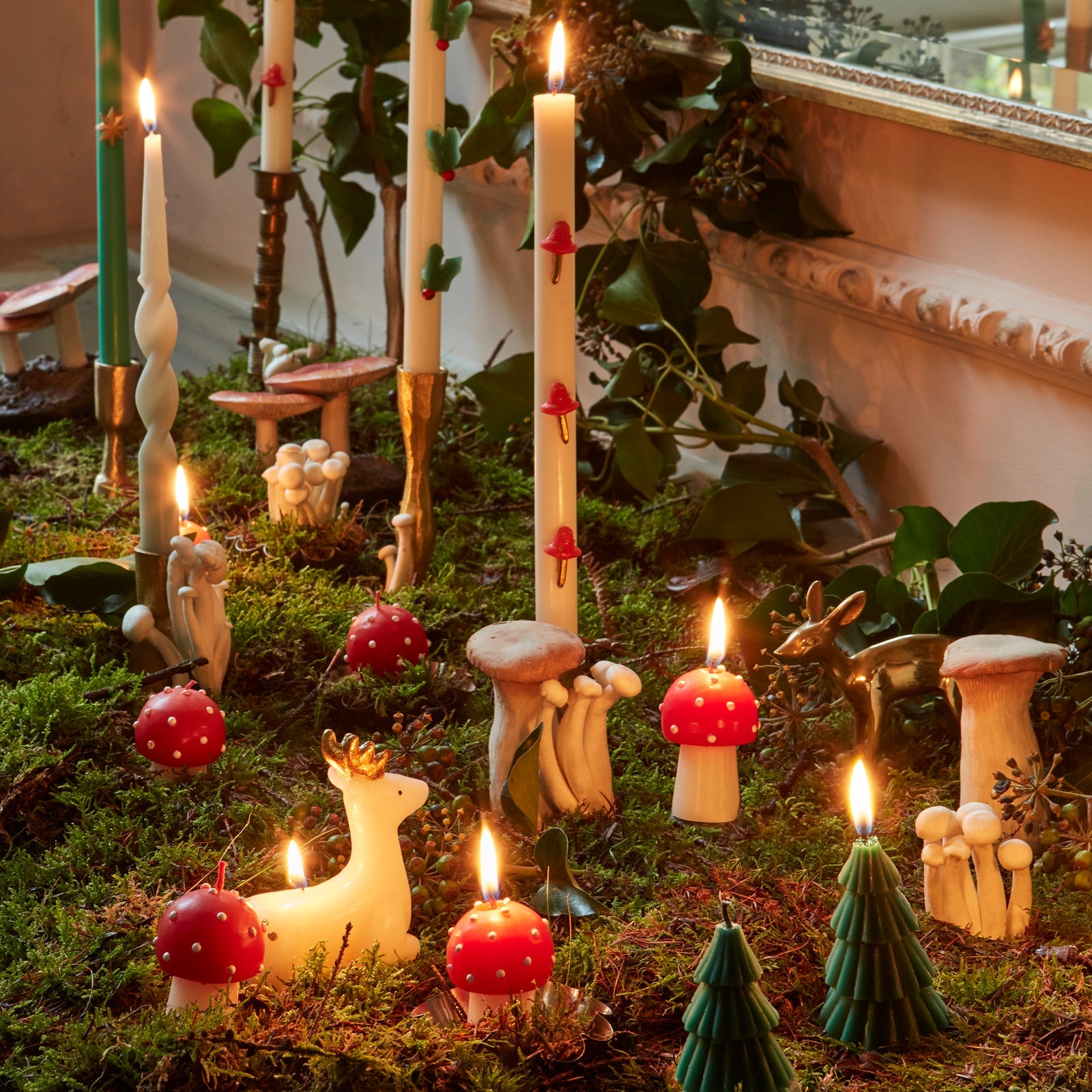 Fairy garden with candles, mushrooms, and small figurines on a grassy surface.