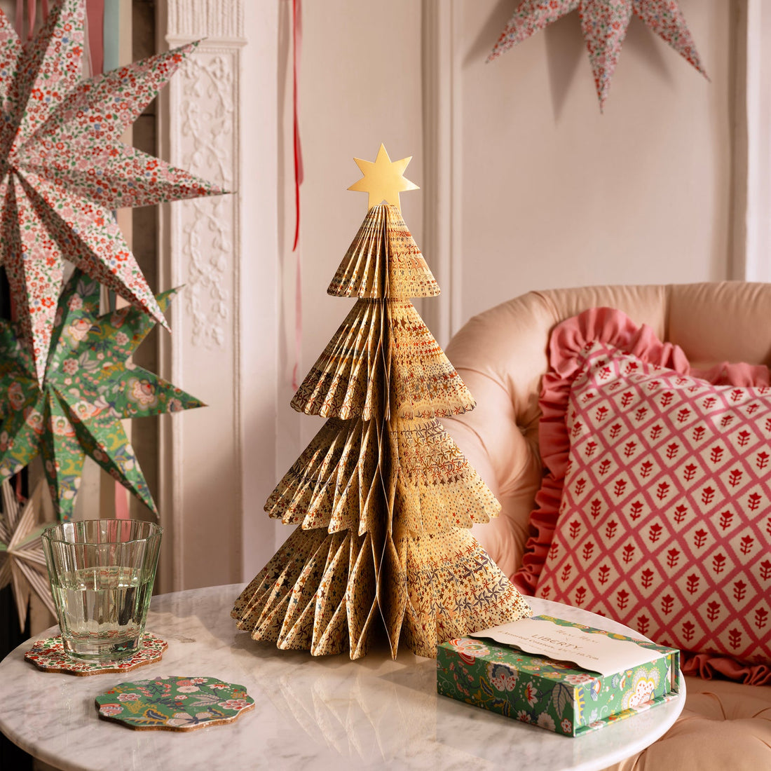 Decorative paper Christmas tree on a table with festive decorations in the background.