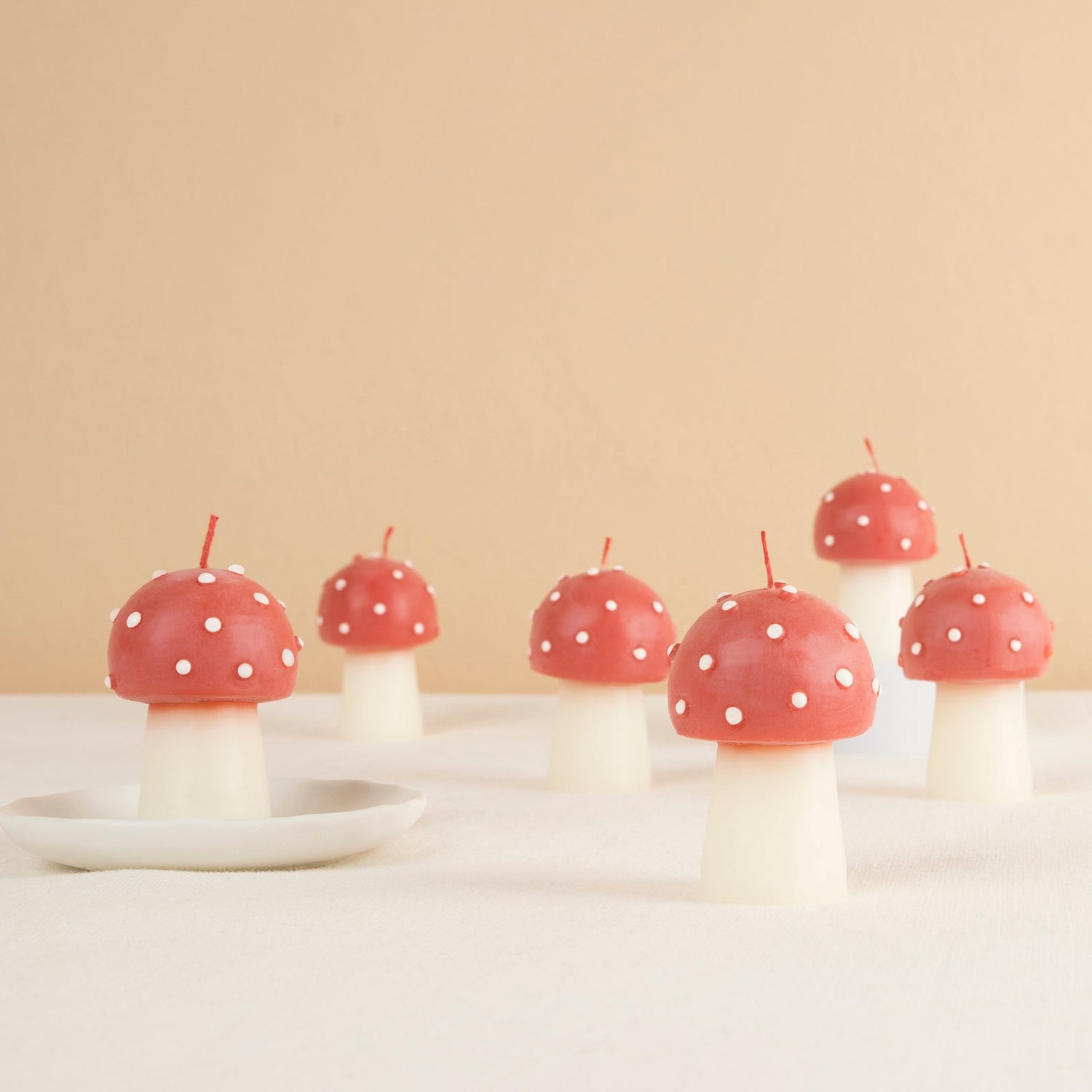 Red and white polka dot mushroom-shaped candles on a beige background.