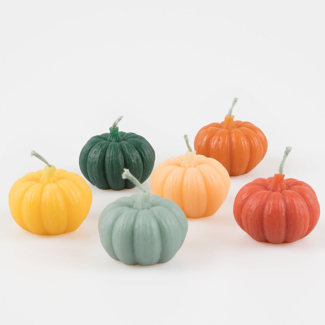 A set of six pumpkin-shaped candles in various autumn colors, presented on a white background.