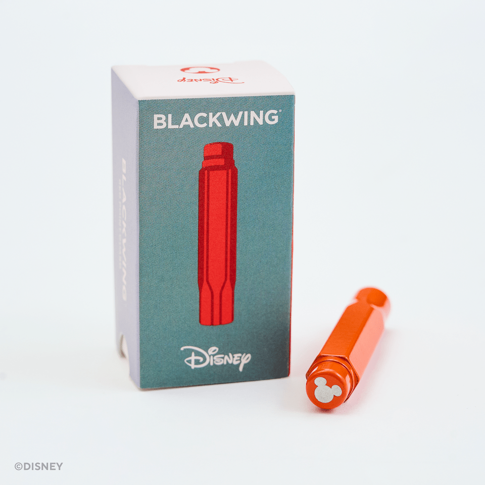 Disney Blackwing point guard and its packaging box on a clean white background. The point guard is bright orange with a Mickey Mouse-shaped tip, and the box is teal with a red marker illustration and Disney branding.