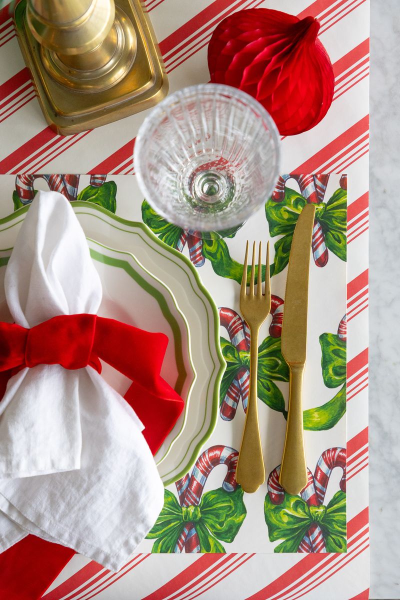 Christmas-themed table setting with candy canes, gold cutlery, and red napkins on a striped tablecloth.