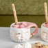 Two Mint/Pink Papa Noel mugs with cookies on a table by Glitterville.