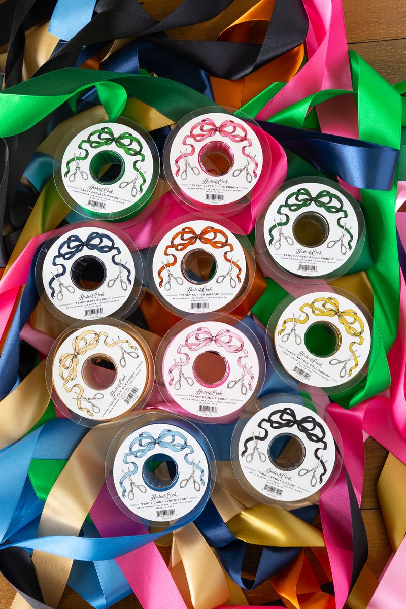 Several spools of satin ribbon in a variety of colors unraveled on a wooden table.