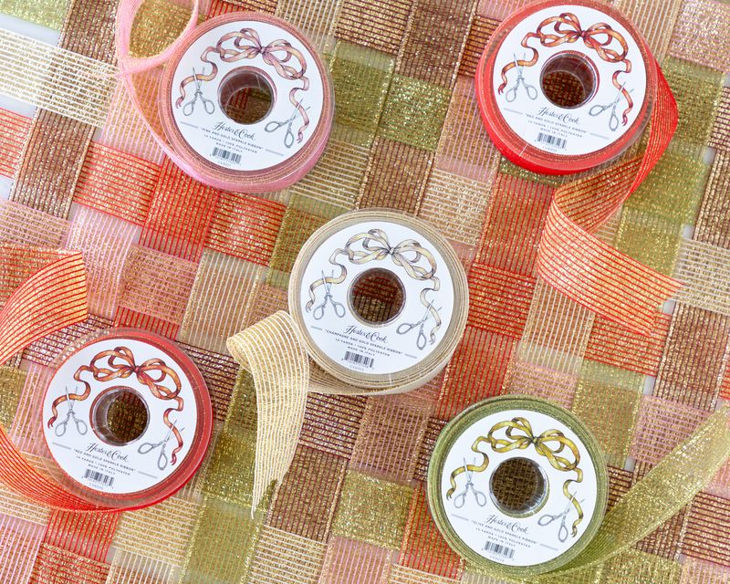 Several spools of sparkly ribbon in various colors unraveled on a surface of woven sparkle ribbon. 