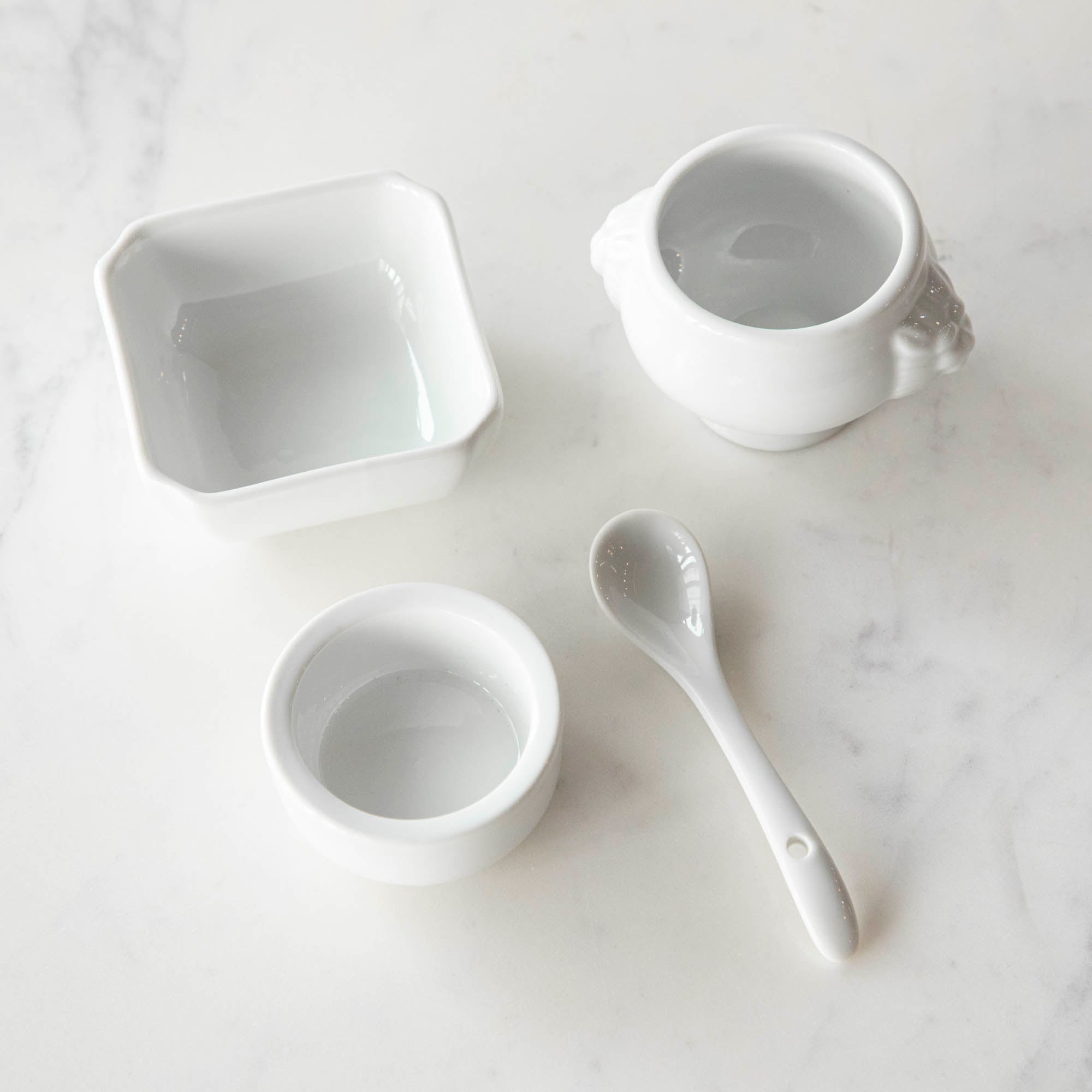 Three White Porcelain Mini Bowls with assorted spices and a spoon on a marble surface by BIA.
