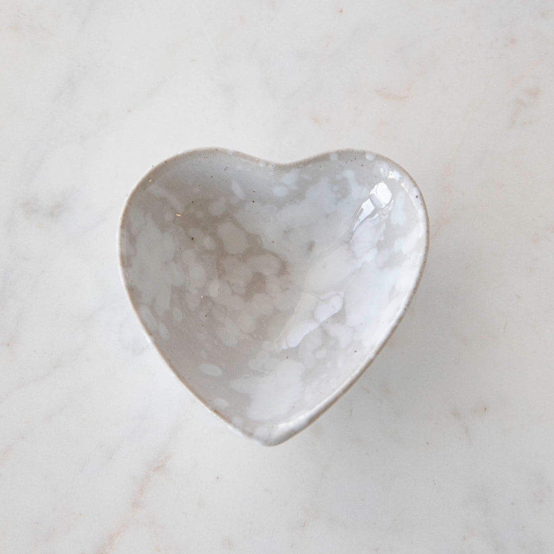 A small Stoneware Heart Dish by Creative Co-Op on a marble surface.