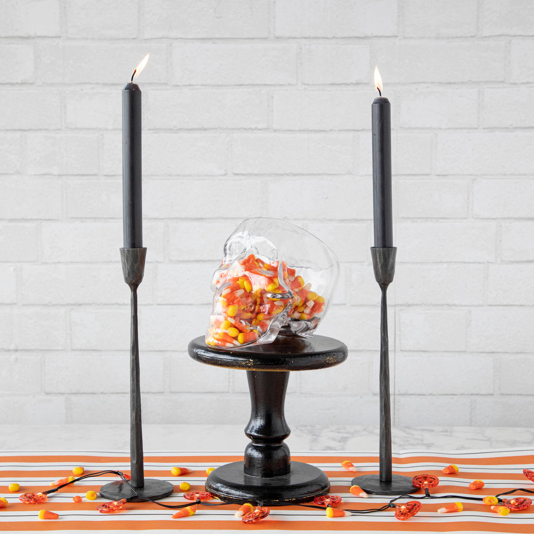 Two black candles on a table with a skull-shaped glass Reaper Pot terrarium from Accent Decor and candy canes on top.
