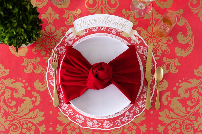 A holiday place setting with a wide soft red ribbon tied like a bow around the plate. 