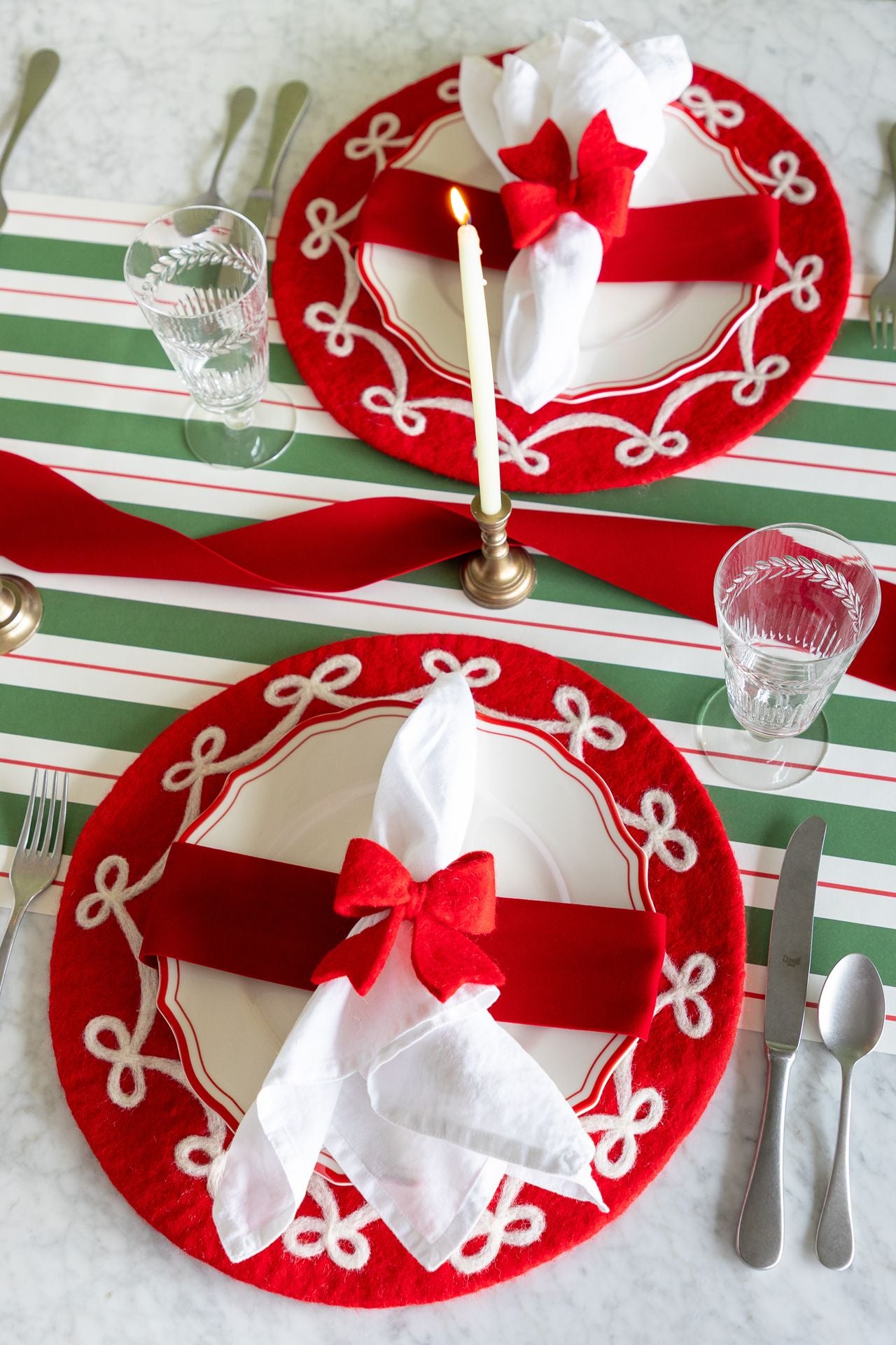 A holiday place setting with red and green decorative elements including a red ribbon wrapped around the plate. 