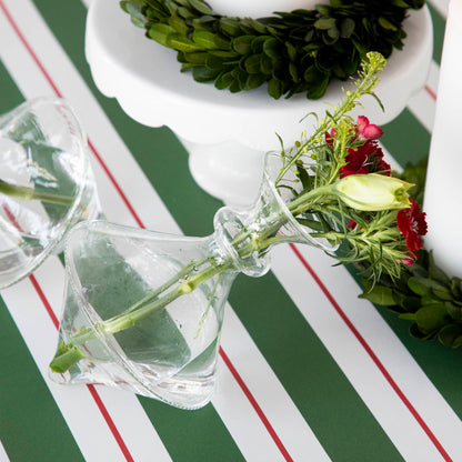 Two Qualia mouth blown clear vases showcasing small bouquets on a green and white striped table.