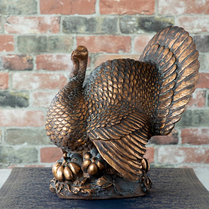 An Antiqued Bronze Turkey Centerpiece with intricate detailing and pumpkins near its base.