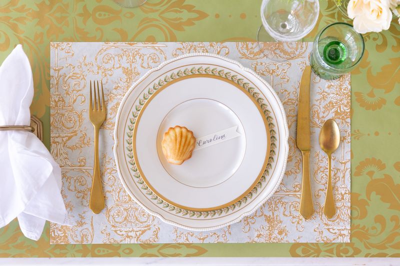 Elegant table setting with gold and white plates, cutlery, and a decorative placemat.