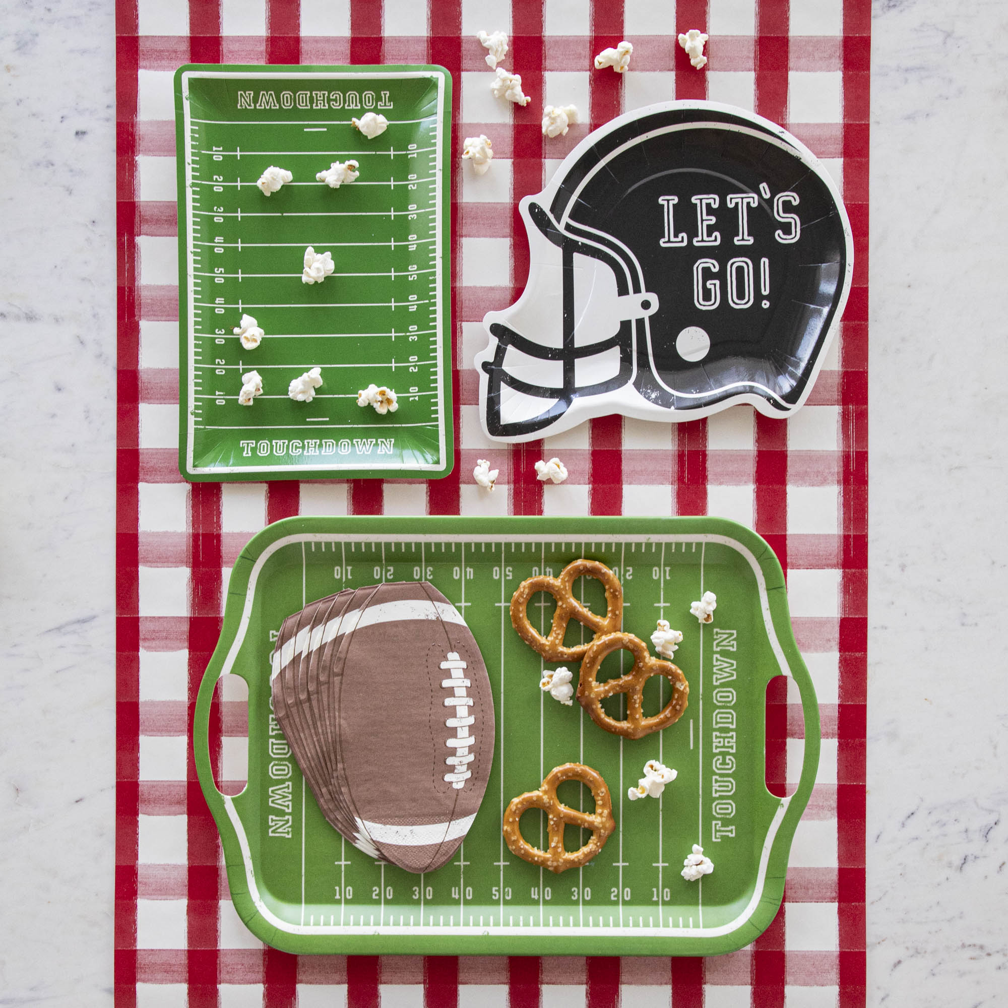 Football themed paper plates with various snacks on a red painted check runner.