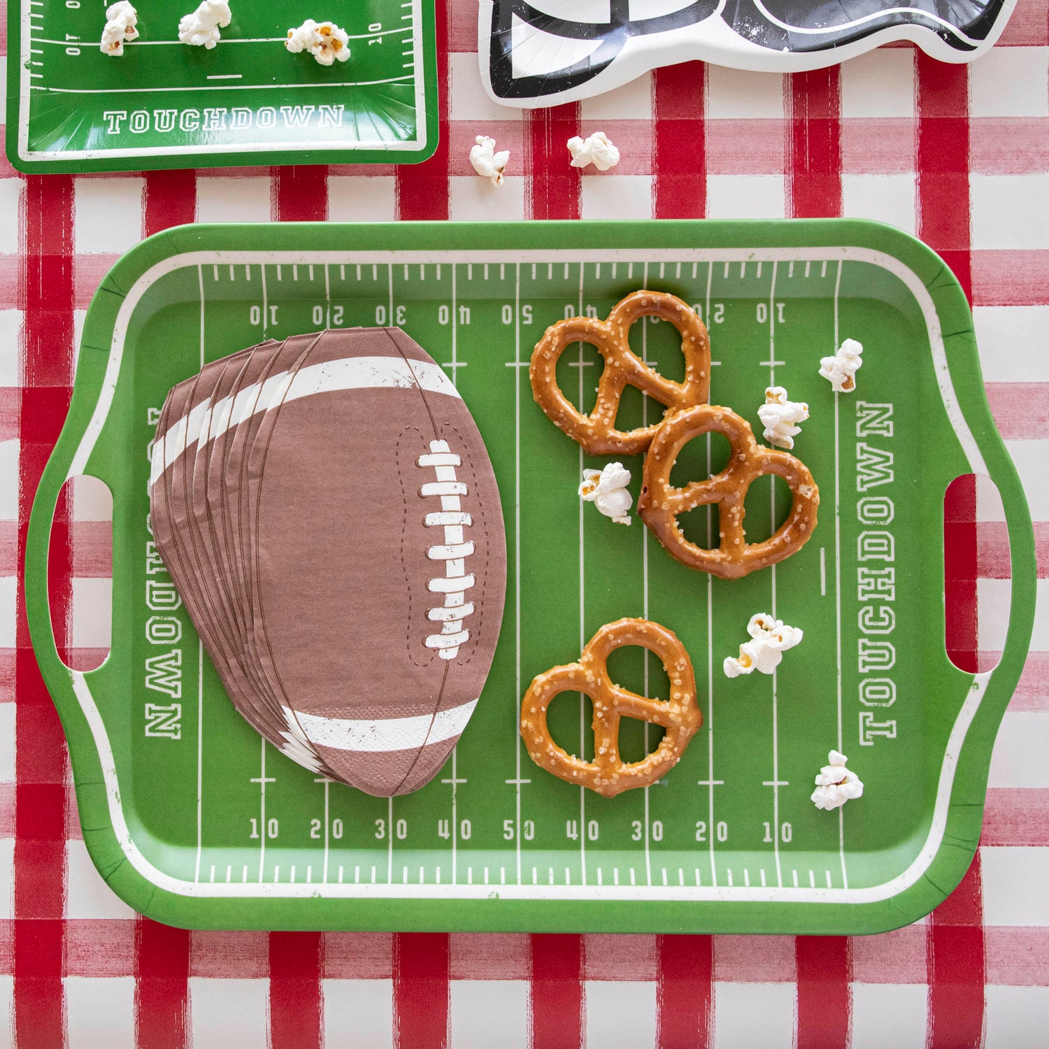 Snacks and die-cut football napkins on top of a football field bamboo reusable tray.