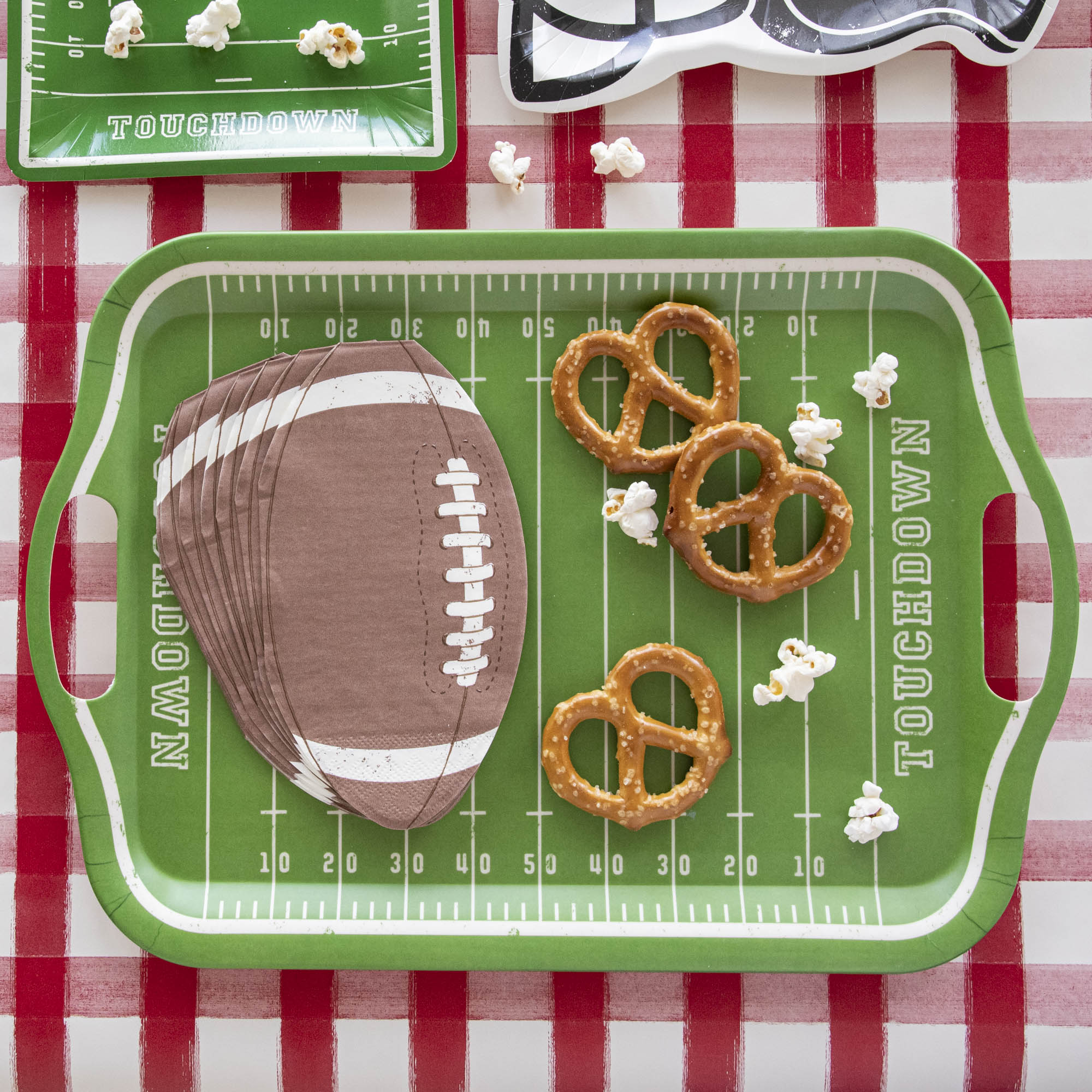 Snacks and die-cut football napkins on top of a football field bamboo reusable tray.