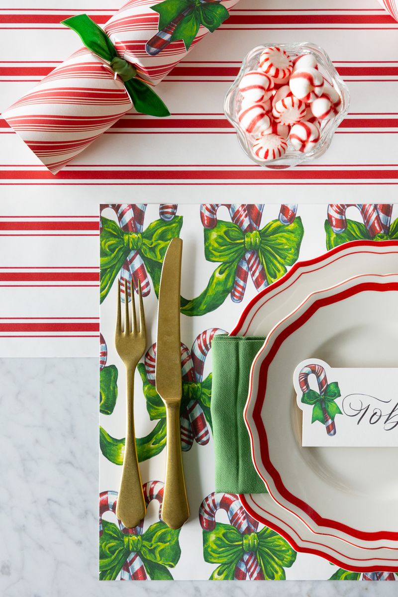 Christmas-themed table setting with candy cane and bow design on a striped tablecloth.
