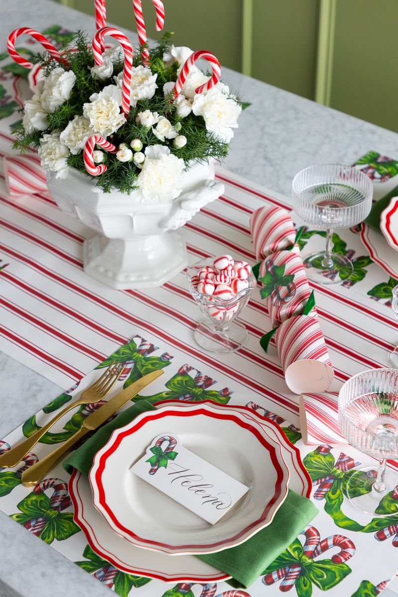 Christmas table setting with floral arrangement, candy canes, and place cards on a striped tablecloth.