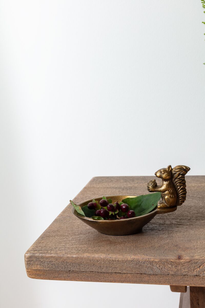 Brass squirrel dish with berries on a wooden surface