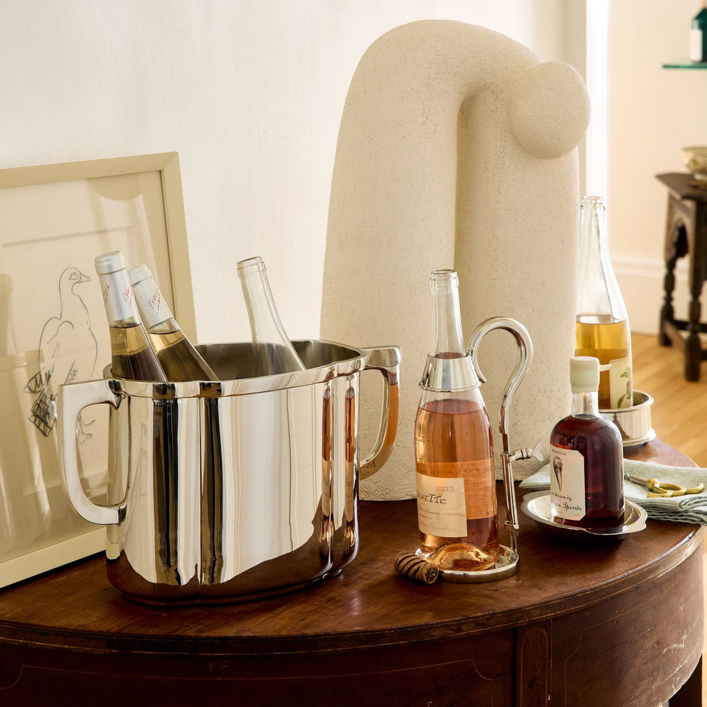 Silver ice bucket with bottles on a wooden table in a room setting.