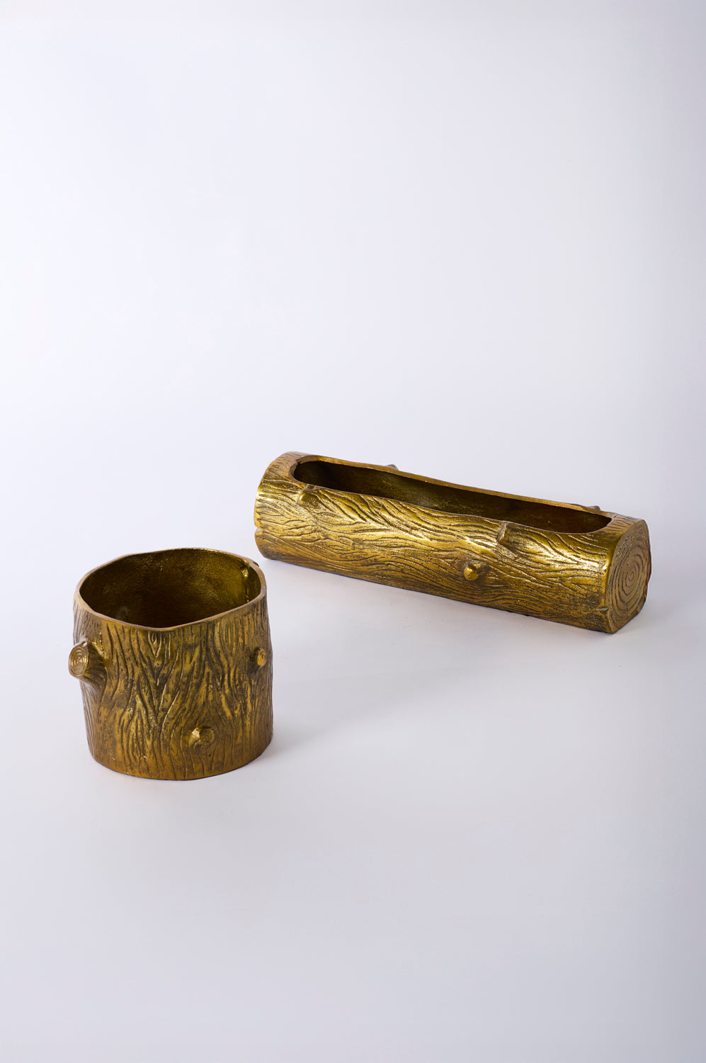 Two brass containers with tree bark design on a white background.