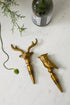 Two brass bottle stoppers shaped like a deer and an owl on a marble surface with a bottle in the background.