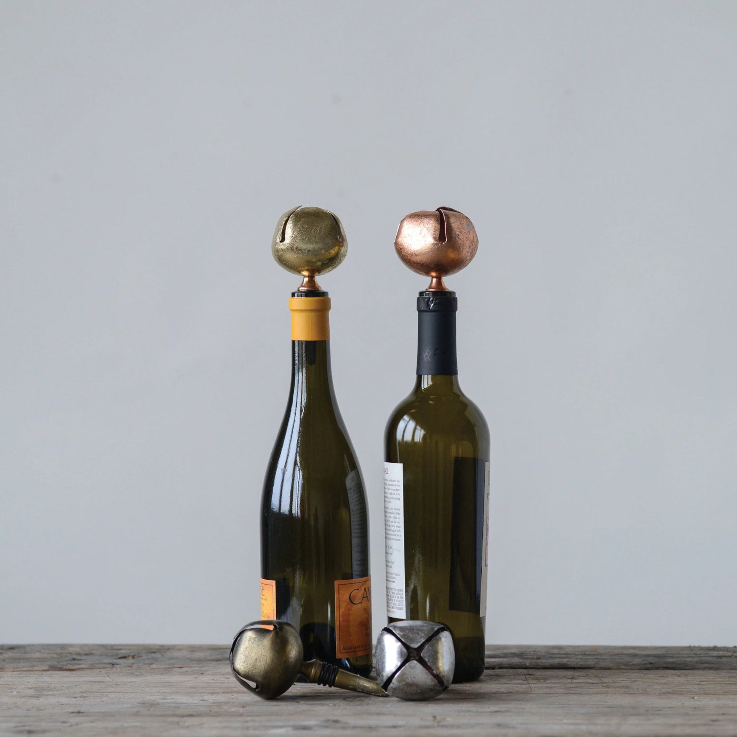 Four metal bottle stoppers with bell designs, in silver, bronze, gold, and black colors, two in bottles. 