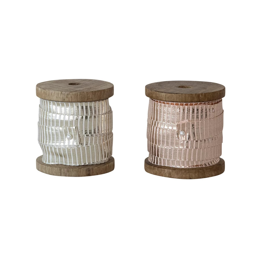 Two wooden spools of metallic ribbon in silver and pink on a white background.